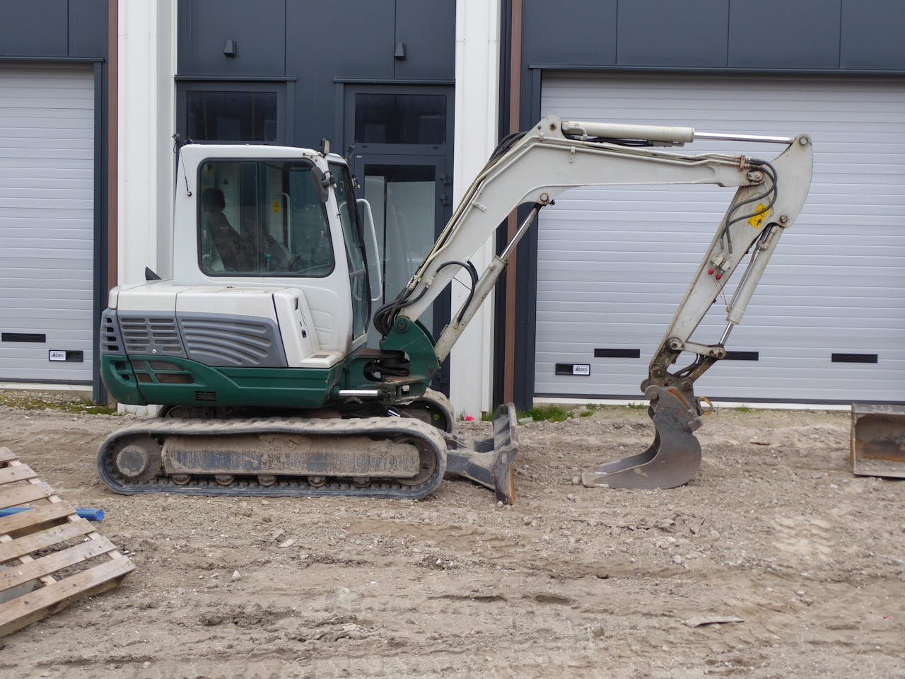 services-03 Side view of a compact excavator on a construction site in front of a building.