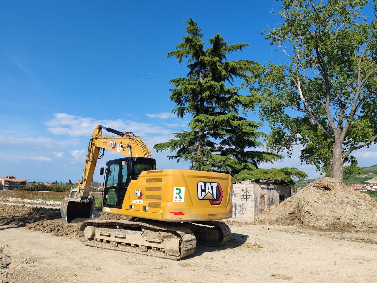services-04 A CAT excavator working at a construction site with trees and blue sky in the background.